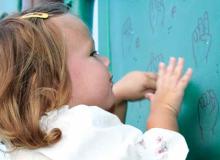 Little girl looking at the ASL alphabet on the wall